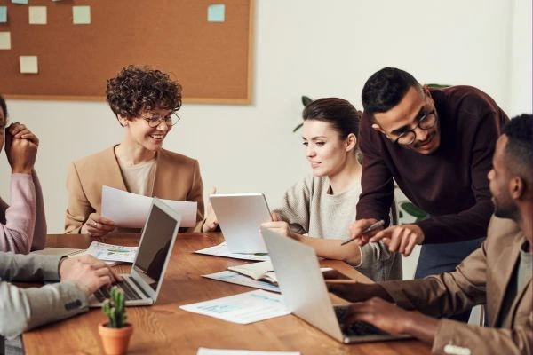 Group of diverse young professionals collaborating in a modern workspace with laptops and documents.