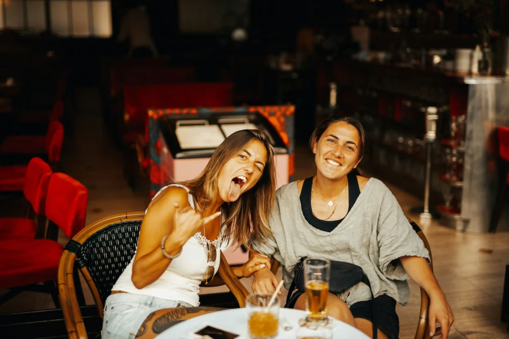 Two young women smiling and laughing over drinks at a bar, enjoying Madrid nightlife and student life.