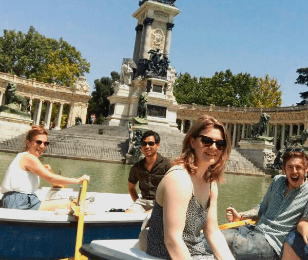 Group of international students rowing a boat at El Retiro Park in Madrid, enjoying a sunny day outdoors.