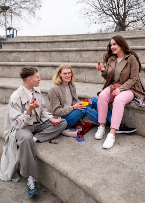 Three postgraduate students talking and sharing fruit outdoors in Madrid, representing the social and collaborative learning lifestyle at BLC Spain.