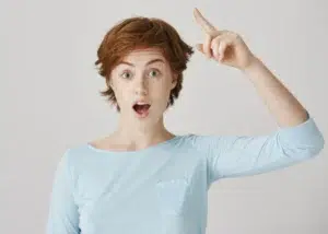A young woman with short red hair and freckles looking surprised and inspired, pointing her finger up as if she just had a breakthrough idea.