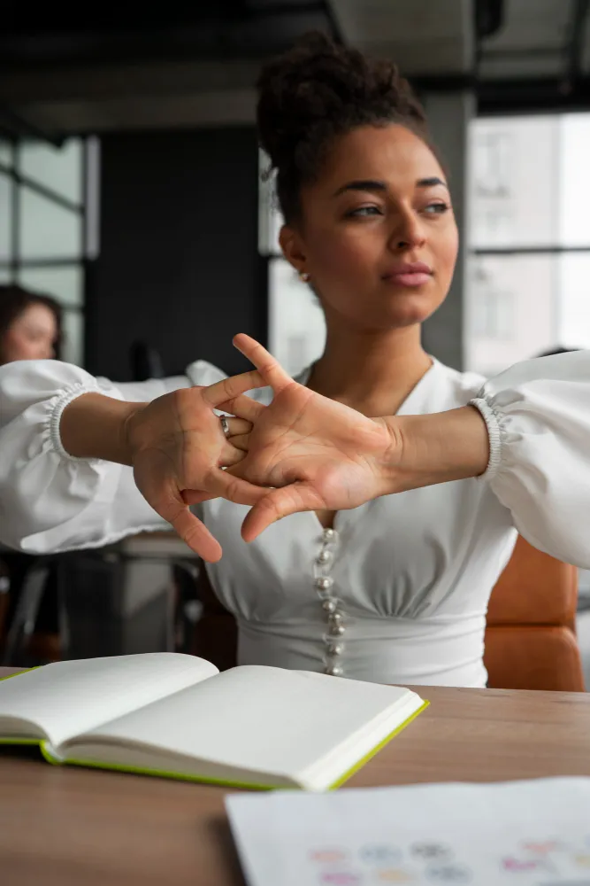 A professional woman in a white blouse stretching at her desk to manage cognitive energy and reduce cortisol levels.
