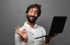 A man with a smug, overly confident expression holding a laptop and making an OK hand gesture, illustrating validation bias and the illusion of agreement when using artificial intelligence.