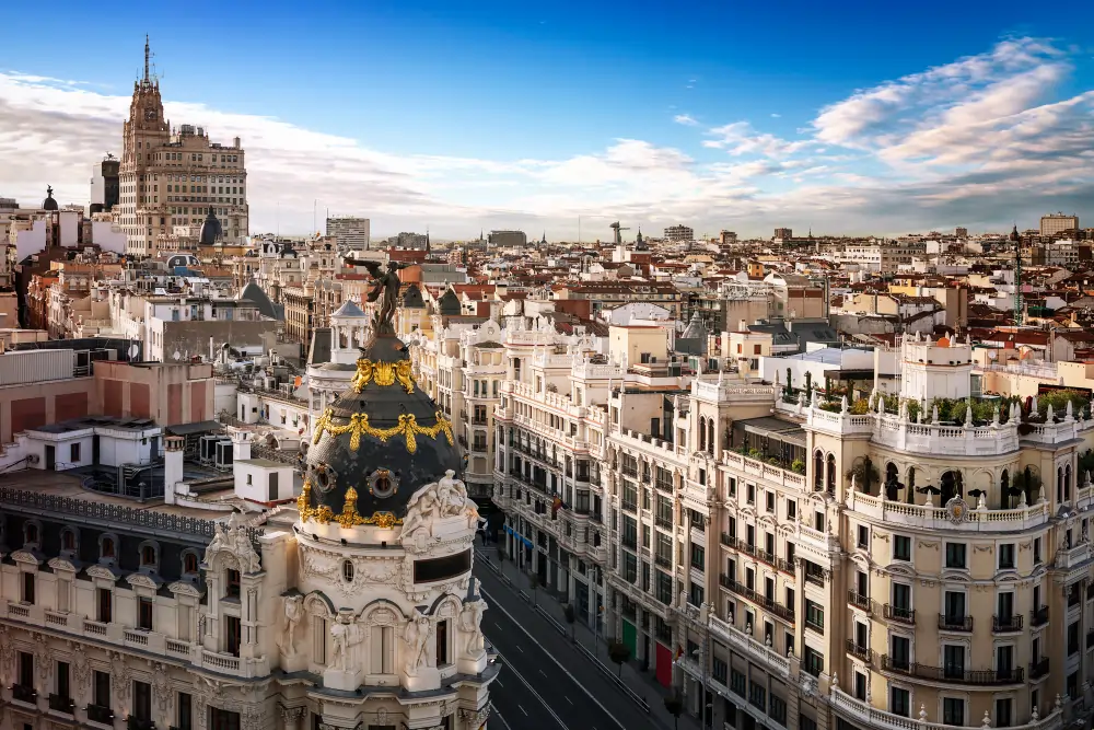 stunning high-angle panoramic view of the Madrid city skyline, showcasing the historic architecture of Gran Vía and the iconic Metropolis building dome under a blue sky.