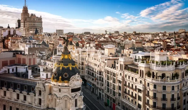stunning high-angle panoramic view of the Madrid city skyline, showcasing the historic architecture of Gran Vía and the iconic Metropolis building dome under a blue sky.