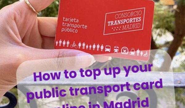 Hand holding a red Madrid public transport card (tarjeta transporte público) with trees in the background.