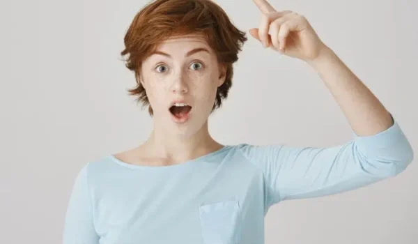 A young woman with short red hair and freckles looking surprised and inspired, pointing her finger up as if she just had a breakthrough idea.