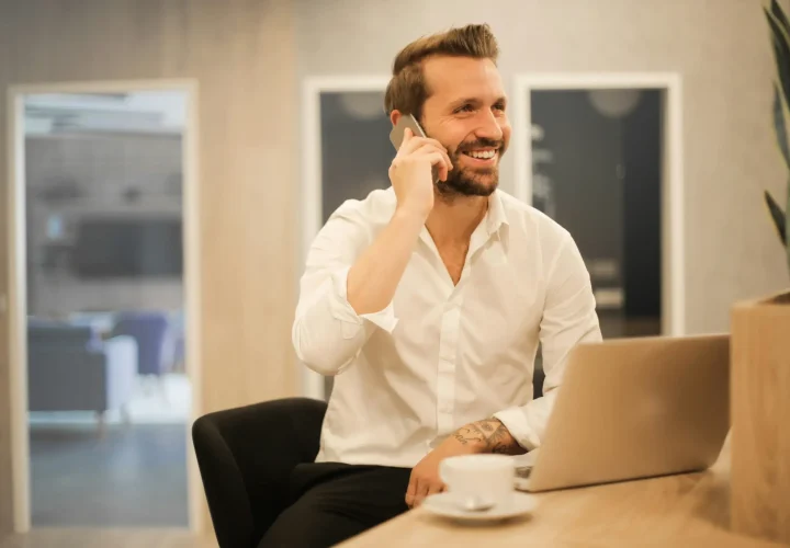 A male professional smiling while taking a business call in a modern Madrid café, reflecting the BLC focus on real-life learning.