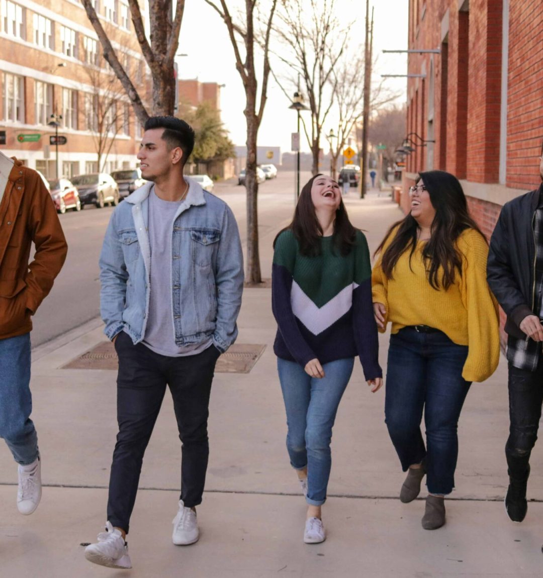 Five friends walking and laughing on a city street.