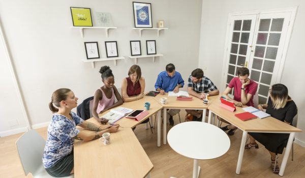 Adult students participating in a Spanish language class at LAE Madrid, seated around a collaborative table in a modern classroom