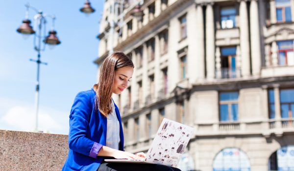 Woman sits on the street and works with a laptop